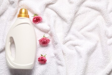 Bottle of fabric softener and flowers on terry towel, flat lay. Space for text