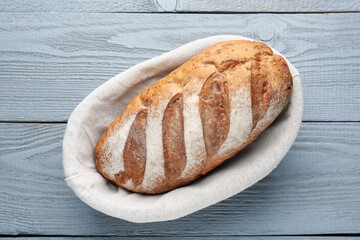 Loaf of bread in basket on grey wooden table, top view