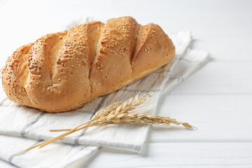 Fresh bread loaf and spikelets on white wooden table, closeup. Space for text