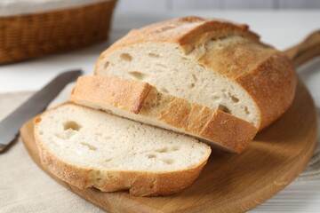 Cut bread loaf and knife on white wooden table, closeup