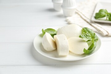 Pieces of delicious mozzarella cheese and basil on white wooden table. Space for text