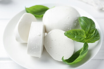Pieces of delicious mozzarella cheese and basil on white wooden table, closeup