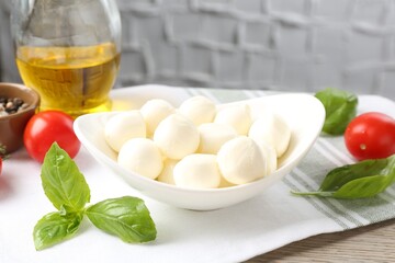 Tasty mozzarella cheese balls, tomatoes, basil, oil and peppercorns on wooden table, closeup