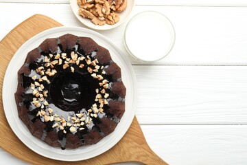 Delicious chocolate bundt cake with nuts and glass of milk on white wooden table, flat lay. Space for text