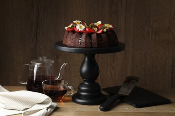 Delicious chocolate bundt cake with strawberries, chamomile flowers and tea on wooden table