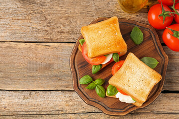 Tasty sandwiches with mozzarella cheese, tomatoes and basil on wooden table, flat lay. Space for text