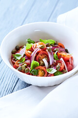 Simple salad with cherry tomatoes, red onion and fresh herbs. Bright wooden background. Close up.	