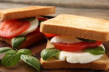 Tasty sandwiches with mozzarella cheese, tomatoes and basil on table, closeup