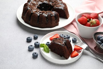 Delicious chocolate bundt cake with strawberries and blueberries on light grey textured table, closeup