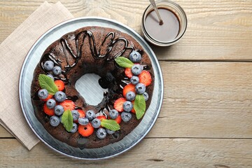 Delicious chocolate bundt cake with strawberries, mint and blueberries on wooden table, flat lay. Space for text