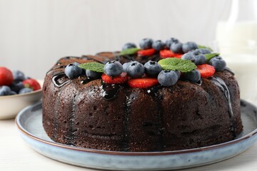 Delicious chocolate bundt cake with strawberries, mint and blueberries on light wooden table, closeup