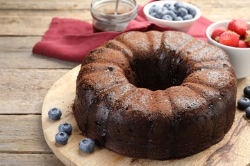 Delicious chocolate bundt cake with blueberries on wooden table, closeup