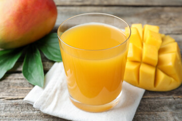 Tasty mango juice in glass, fresh fruits and green leaves on wooden table, closeup