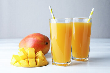 Tasty mango juice in glasses and fresh fruits on white wooden table, closeup