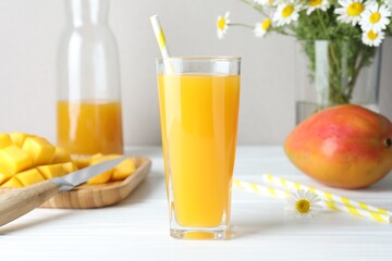 Tasty mango juice in glass, fresh fruits and chamomile flowers on white wooden table, closeup