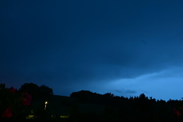Dramatic stormy clouds gathering over a hilly landscape with heavy rain falling in the distance.