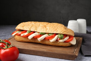 Tasty sandwich with mozzarella cheese, tomatoes and basil on grey textured table against dark background, closeup
