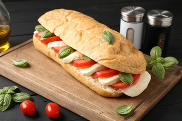 Tasty sandwich with mozzarella cheese, tomatoes and basil on black wooden table, closeup
