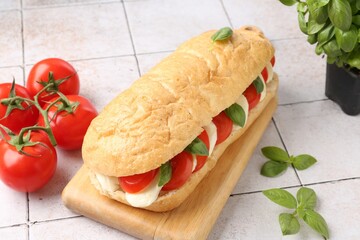Tasty sandwich with mozzarella cheese, tomatoes and basil on light tiled table, closeup