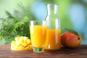 Tasty mango juice in glass, carafe and fresh fruits on wooden table against blurred background