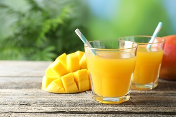 Tasty mango juice in glasses and fresh fruits on wooden table against blurred background, closeup. Space for text
