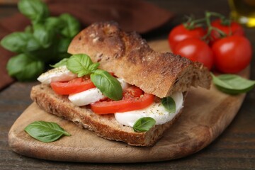 Tasty sandwich with mozzarella cheese, tomatoes and basil on wooden table, closeup