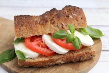 Tasty sandwich with mozzarella cheese, tomatoes and basil on white wooden table, closeup