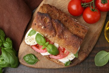 Tasty sandwich with mozzarella cheese, tomatoes and basil on wooden table, flat lay