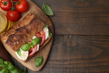 Tasty sandwich with mozzarella cheese, tomatoes and basil on wooden table, flat lay. Space for text