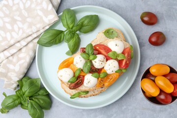 Tasty sandwich with mozzarella cheese, tomatoes and basil on grey table, flat lay