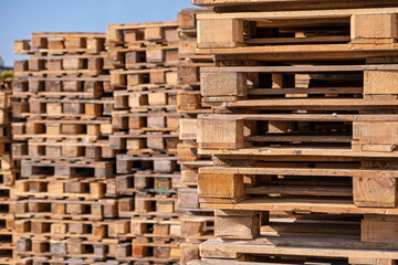 A large number of wooden pallets neatly stacked in an outdoor storage area. Used in logistics, shipping and warehousing industries.