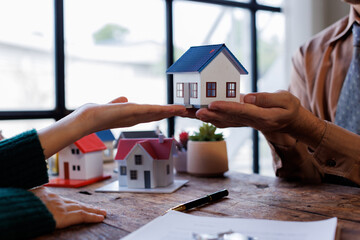 Real estate transaction with agent holding home model, investment small miniature white toy house....