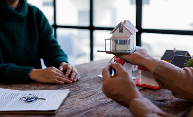 Real estate transaction with agent holding home model, investment small miniature white toy house....
