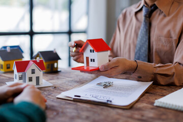 Real estate transaction with agent holding home model, investment small miniature white toy house....
