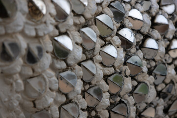 close-up of a textured surface covered in numerous small, silver, semi-circular mirrors embedded in a grey material.
