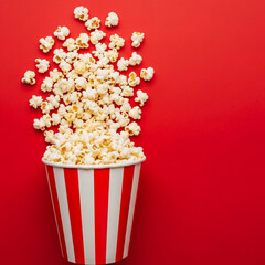 Overflowing Popcorn in a Classic Red and White Striped Bucket on a Vivid Red Background, Perfect for Movie Theaters and Events
