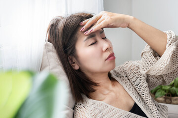 Asian woman feeling dizzy and having a headache, holding her head in pain due to hangover, lack of...
