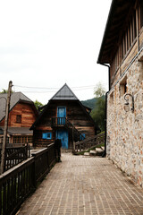 Pathway lined with railings leading to a rustic wooden cabin with vivid blue doors in Drvengrad, Serbia.