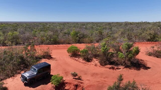 Drone Shot of Couple Waving on Red Sand Beach with Land Rover in Background
