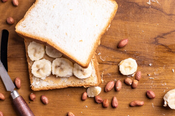 Delicious toast topped with peanut butter, banana slices,Crunchy bread slice with creamy peanut butter and sliced banana, arranged artfully on a clean chopping board with peanuts scattered arround it