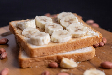 Delicious toast topped with peanut butter, banana slices,Crunchy bread slice with creamy peanut butter and sliced banana, arranged artfully on a clean chopping board with peanuts scattered arround it