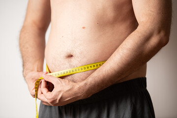A man stands at home measuring his waist with a tape measure, focusing on his health and fitness...