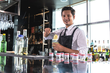 Asian bartender man putting piece of lime into  cocktail glass in bar