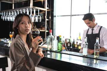 Female Asian office worker drinking glass of wine at counter bar after work