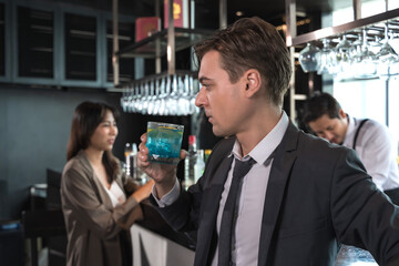 Handsome office man drinking cocktail in rooftop bar after work with female coworker