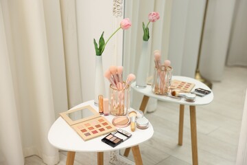 Different makeup products and brushes on white table near mirror indoors