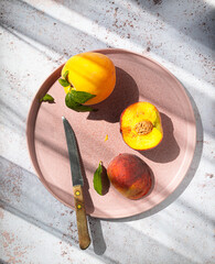 Vibrant peaches and nectarine on a pink plate with a knife, capturing a sunny, fresh, and healthy fruit concept.