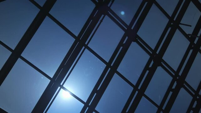 Blue sky with a sun shining through the windows of a building. The sun is casting a shadow on the building