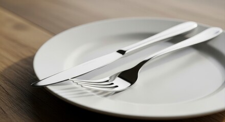 Polished stainless steel fork and knife on a white plate set on a wooden table