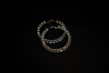Top view of intersecting rhinestone hoop earrings on black background – luxury jewelry composition

